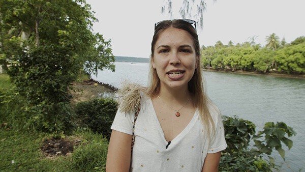 Woman talking to camera by river, lush greenery background