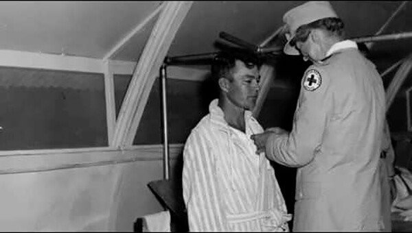 Man in striped robe receives medal from person in uniform with Red Cross emblem.