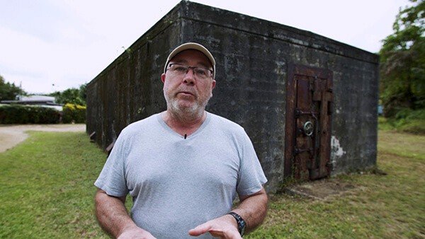Man in front of a concrete bunker with a rusty metal door