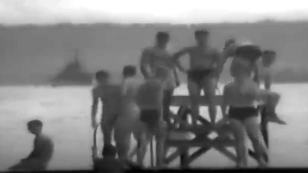 Group of young men in swimsuits on a wooden platform by the water