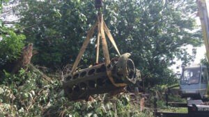 Crane lifting vintage aircraft engine from dense foliage