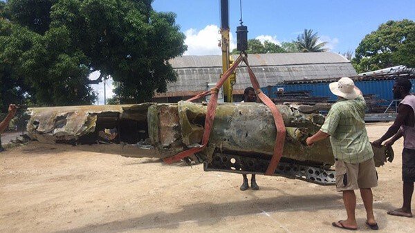Crane lifting large airplane wreckage with workers nearby