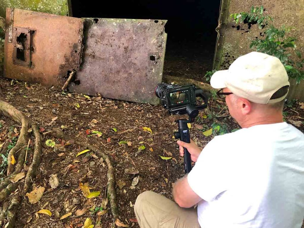 Man filming rusty metal doors of an abandoned bunker entrance.