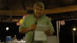 Man in green shirt speaking into microphone at event