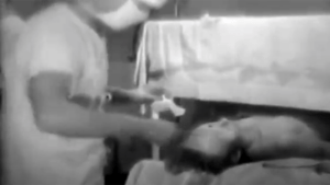 Black and white video still of a person receiving medical attention