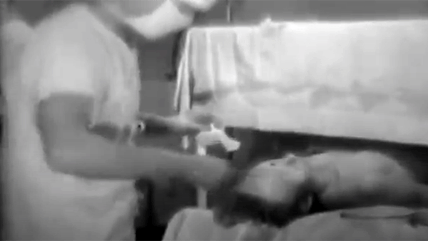 Black and white video still of a person receiving medical attention
