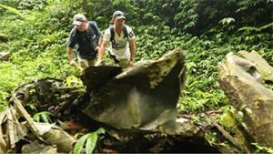 Two explorers examine wreckage in a dense jungle, possibly a plane crash site.