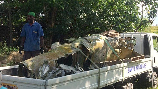 Plane wreckage being loaded onto a truck in a tropical setting.