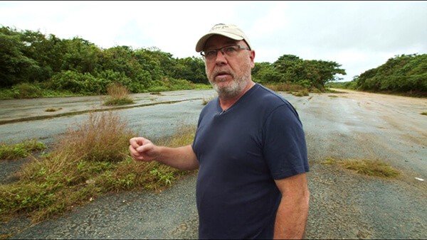 Man in cap and glasses on overgrown road, video context
