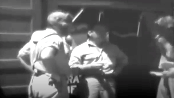 Three people stand near a train car, possibly for a video.