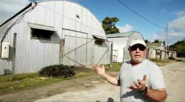Man in front of a corrugated metal building, possibly a warehouse or barn.