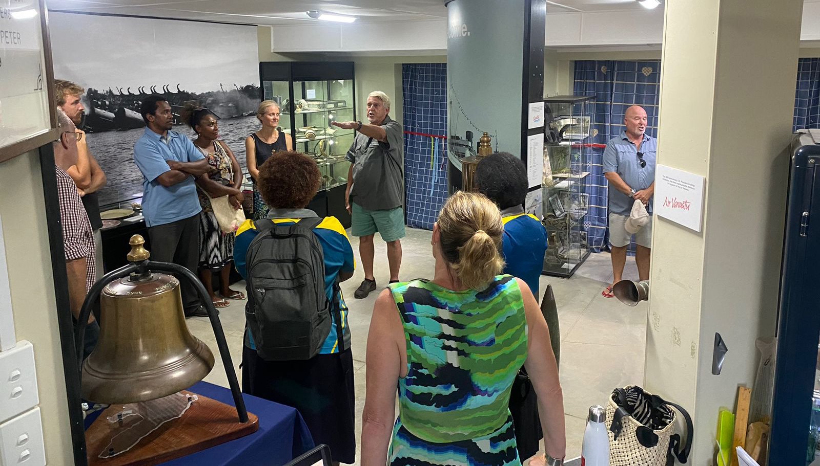 Tour group in a museum gallery, some looking at exhibits, others listening to a guide.