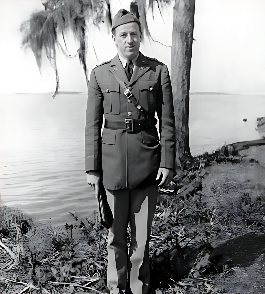 Elwood J Euart in uniform, standing outdoors by water and trees.