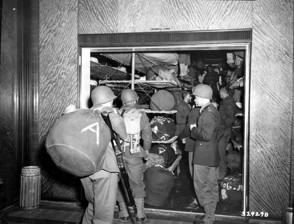 Soldiers in uniform with duffel bags entering a crowded lounge