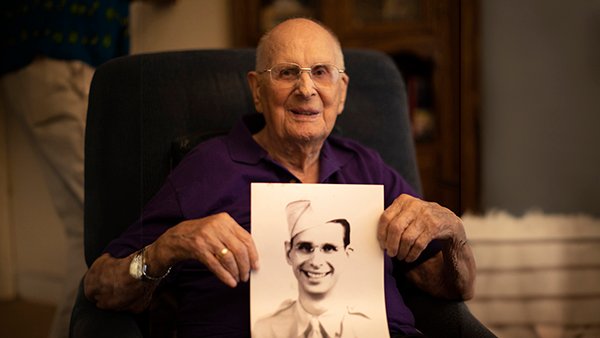 Elderly veteran holding a vintage photo of himself in uniform