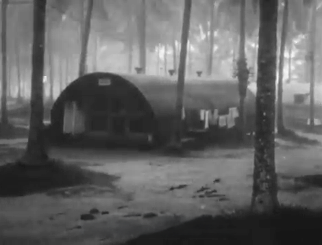 Quonset hut barracks in a tropical forest setting with laundry hanging to dry.